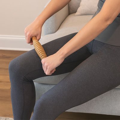 Femme utilisant le rouleau de massage en bois sur ses mollets pour détendre les muscles après l'entraînement