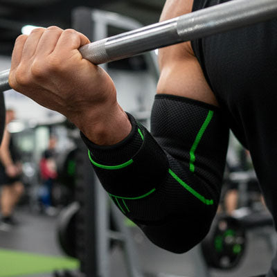 Homme portant un manchon de compression pour coude vert lors d'un Curel à la barre en salle de sport