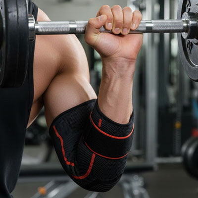 Manchon de compression pour coude avec bandes rouges porté lors d'un exercice de curl à la barre